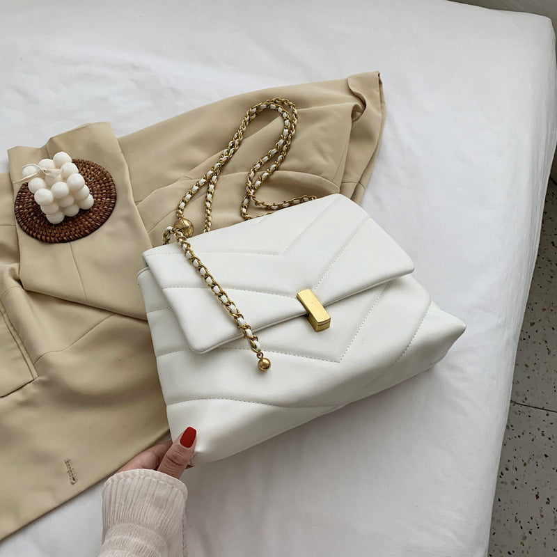 White quilted chain chevron shoulder bag with gold clasp with coat background
