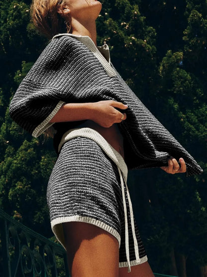 side view of woman wearing a white and black collared contrast striped knit top and matching shorts co-ord lounge set.