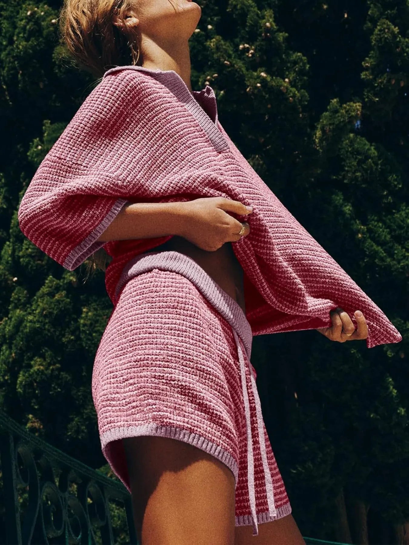 side view of woman wearing a pink collared contrast striped knit top and matching shorts two piece casual set.