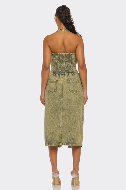 back view of woman wearing green acid wash halter denim midi dress with backless design and front slit