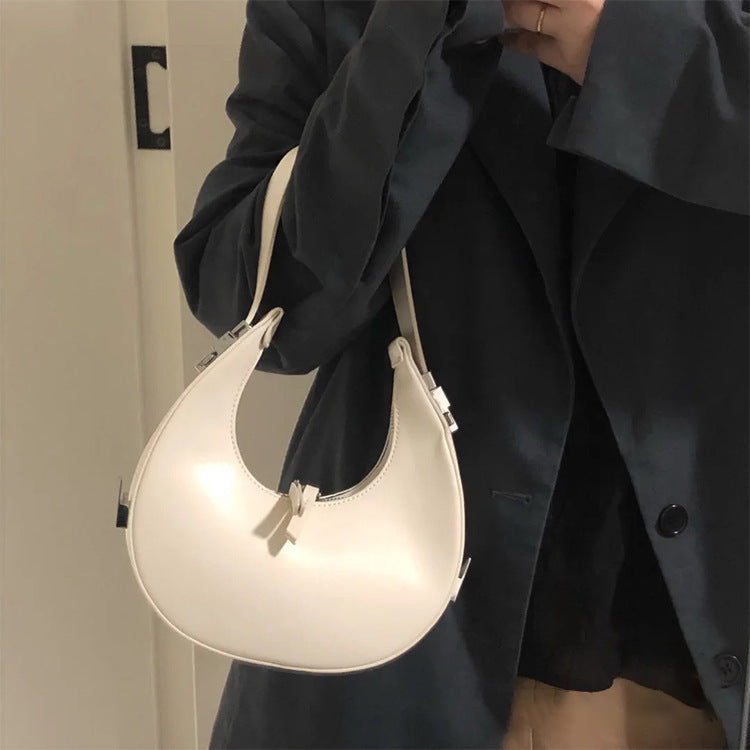 Woman holding a beige/off white genuine leather crescent mini handbag against a neutral background