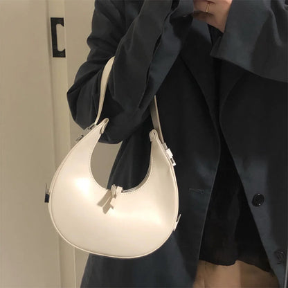 Woman holding a beige/off white genuine leather crescent mini handbag against a neutral background