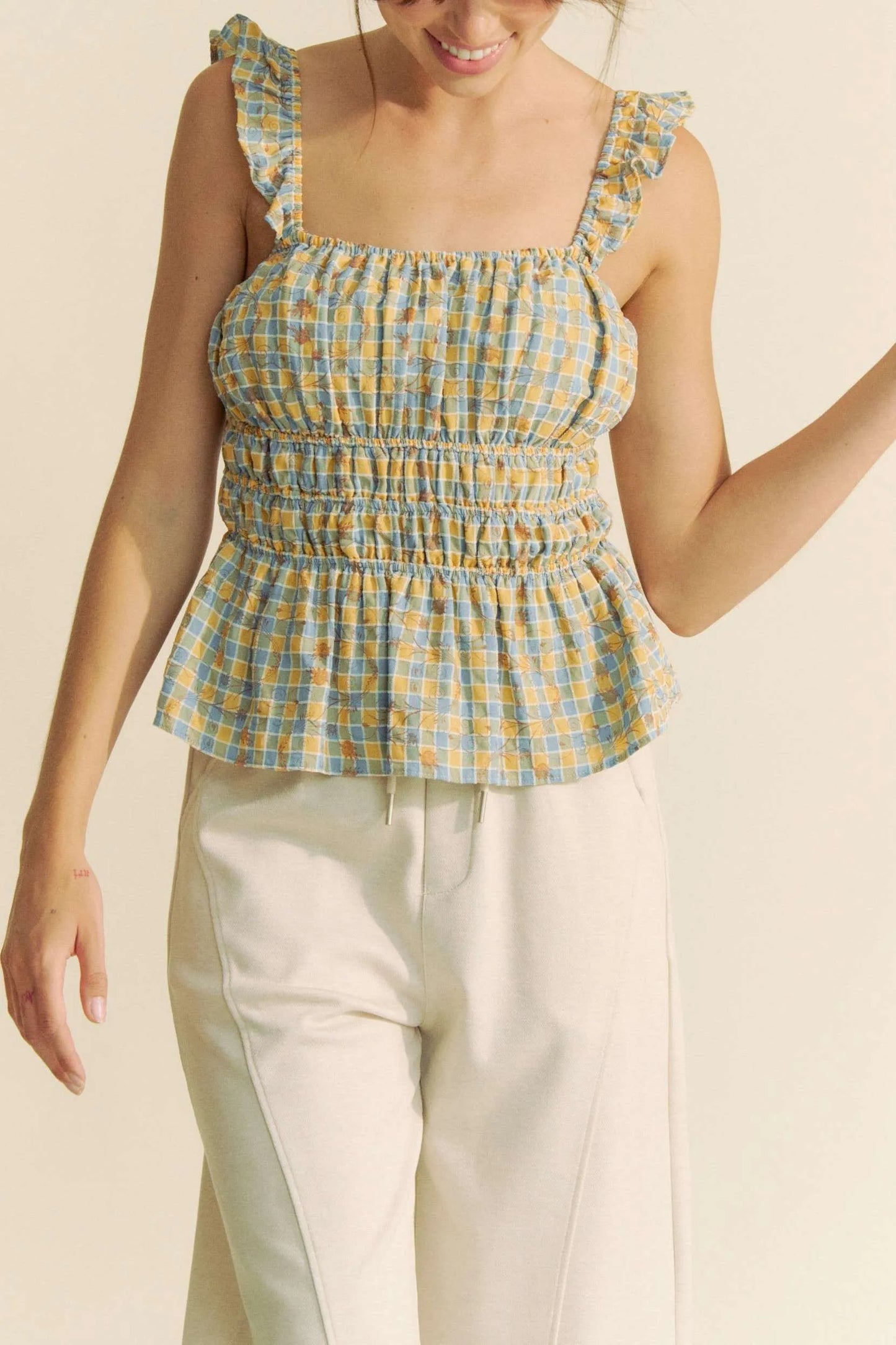 Model wearing plaid smocked top with ruffle straps front view in a neutral background
