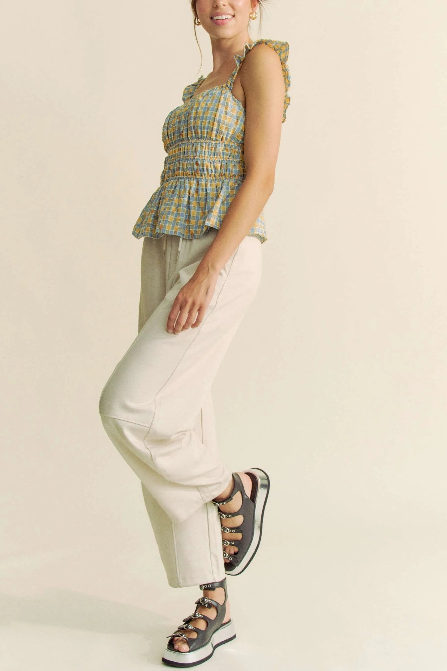 Model wearing plaid smocked top with ruffle straps side view with pants