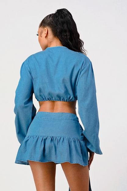 back view of woman wearing a blue denim tie-front long sleeve crop top and wrap mini ruffle skirt 