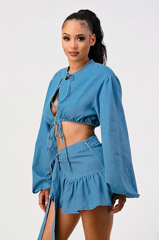 side profile of woman wearing a blue denim tie-front long sleeve crop top and wrap mini ruffle skirt 