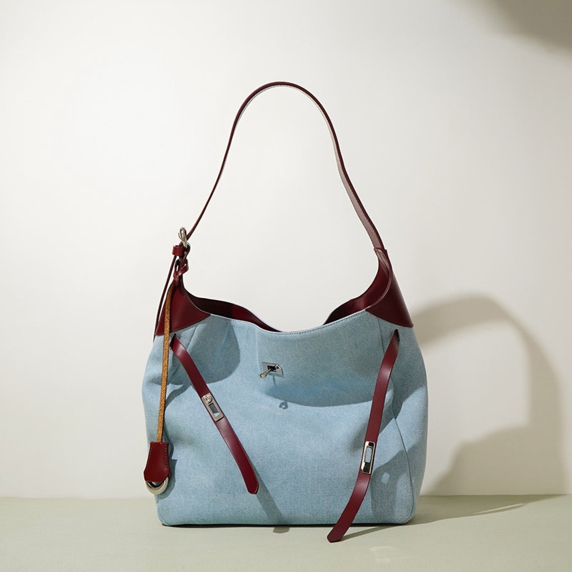 Light blue denim handbag with burgundy genuine leather shoulder straps on a white background