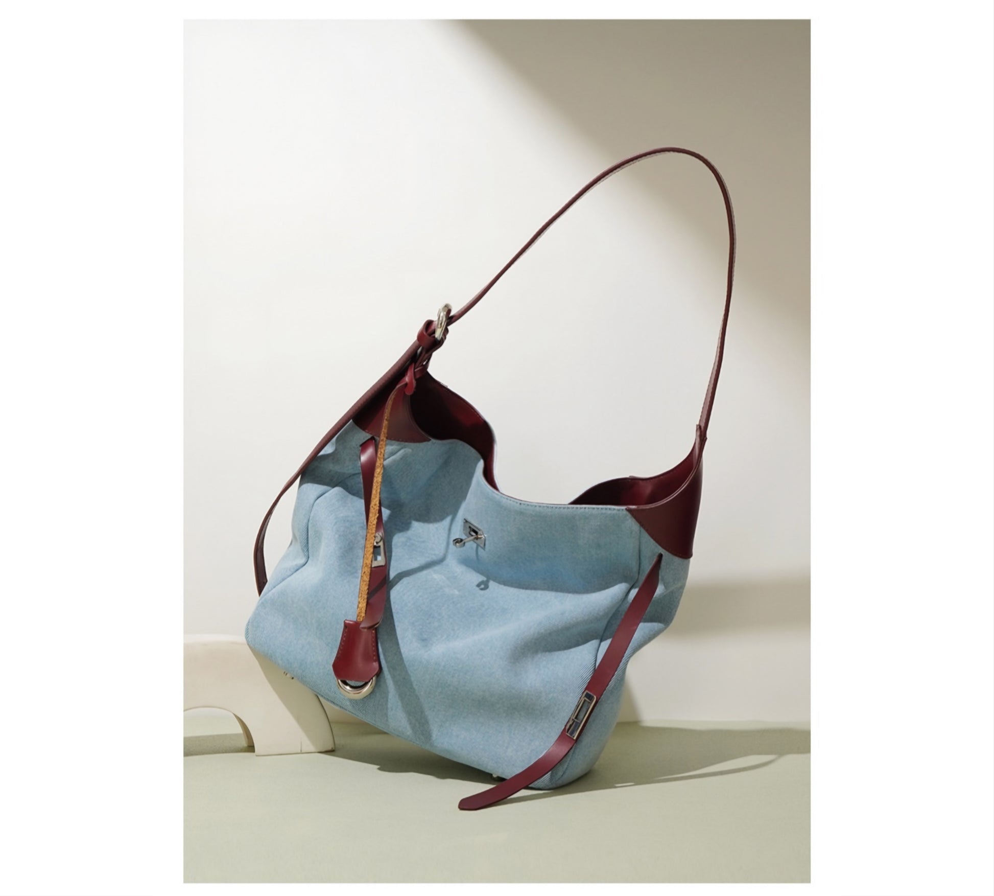 Light blue denim shoulder bag with burgundy genuine leather accents on a light beige background
