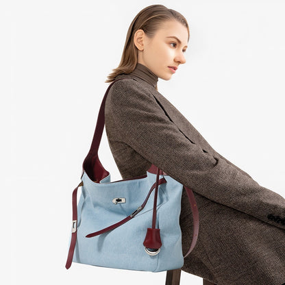 Woman holding a light blue denim shoulder tote bag with burgundy genuine leather straps on a white background
