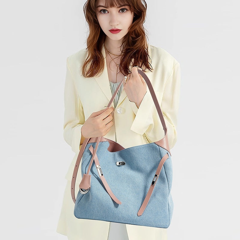 Woman holding a light blue denim shoulder tote handbag with pink genuine leather shoulder straps against a white background