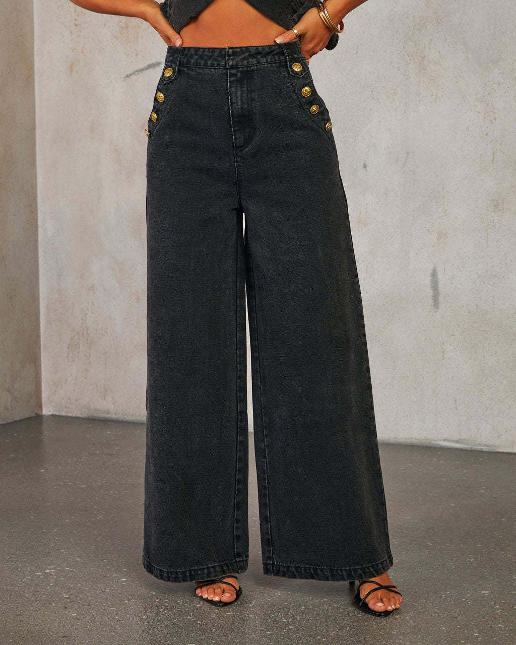 Woman wearing black wide-leg jeans with gold buttons against a neutral background