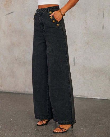 Side view of woman wearing high waist wide-leg black jeans with gold buttons against a plain background
