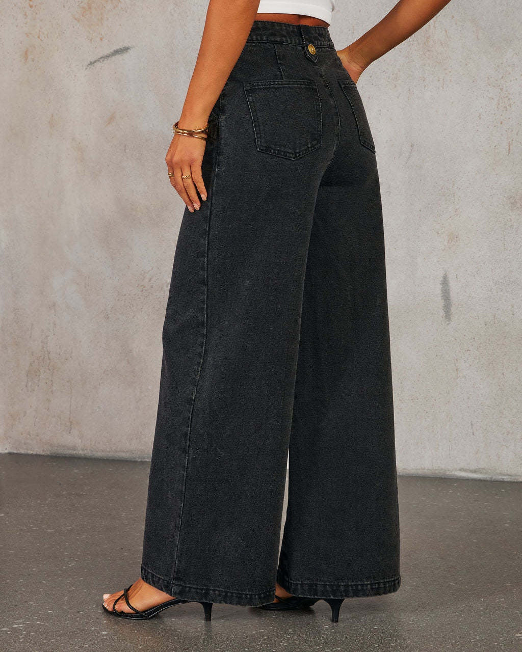 Back view of woman wearing high waist wide-leg black jeans against a plain background