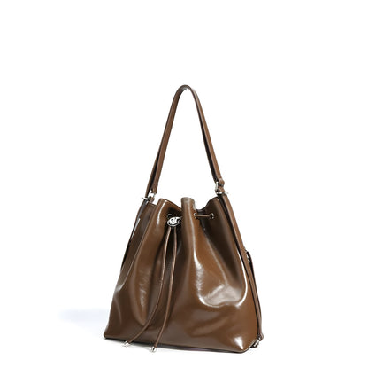 Angle view of brown genuine leather drawstring bucket shoulder handbag on a white background