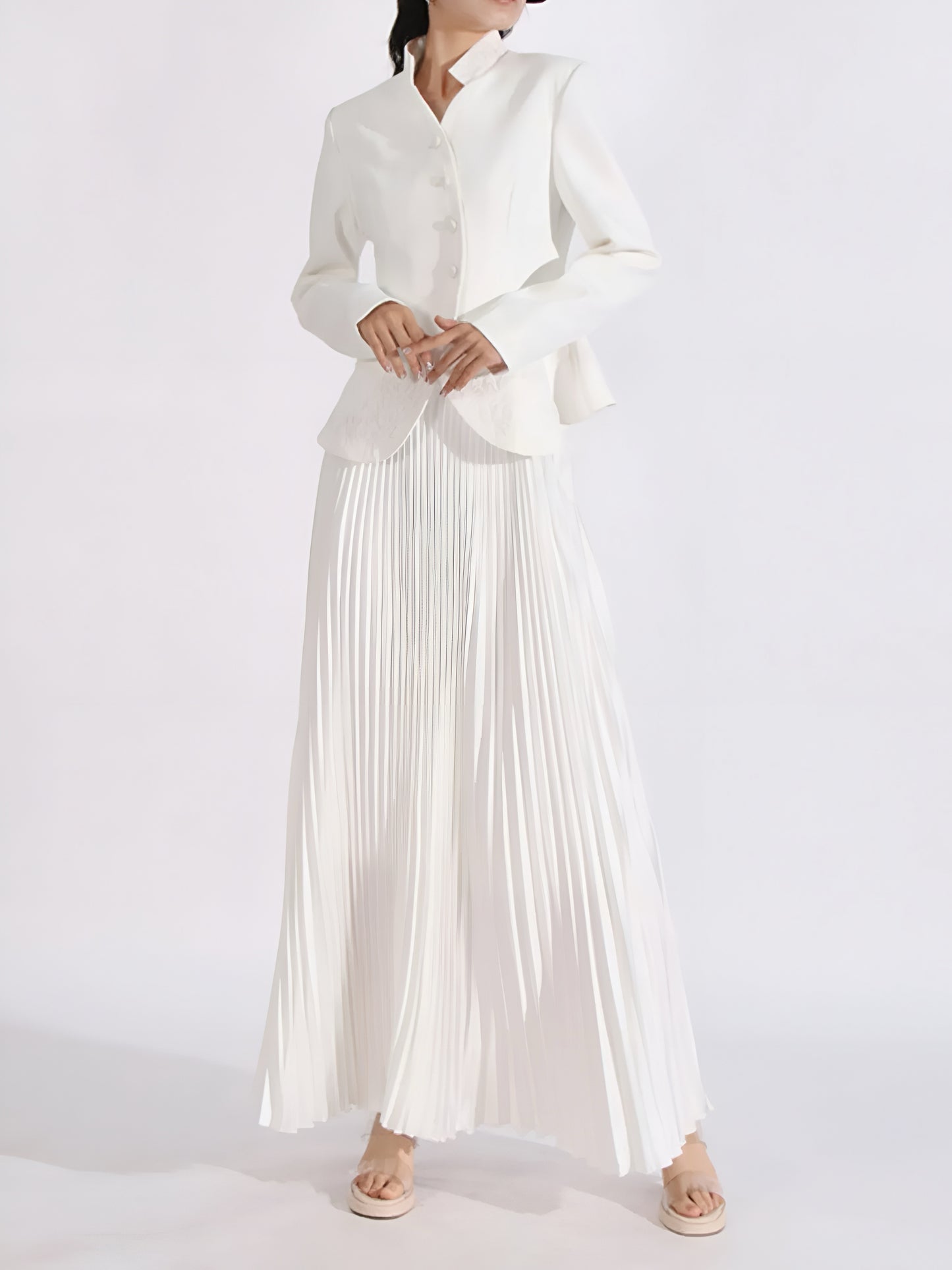 Woman wearing a white pleated maxi skirt set  with a embroidered long sleeve suit blazer on a white background