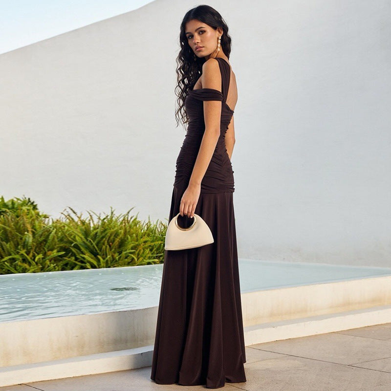 Side view of model wearing elegant one-shoulder  asymmetrical bodycon dark brown formal evenng dress in an outdoor setting
