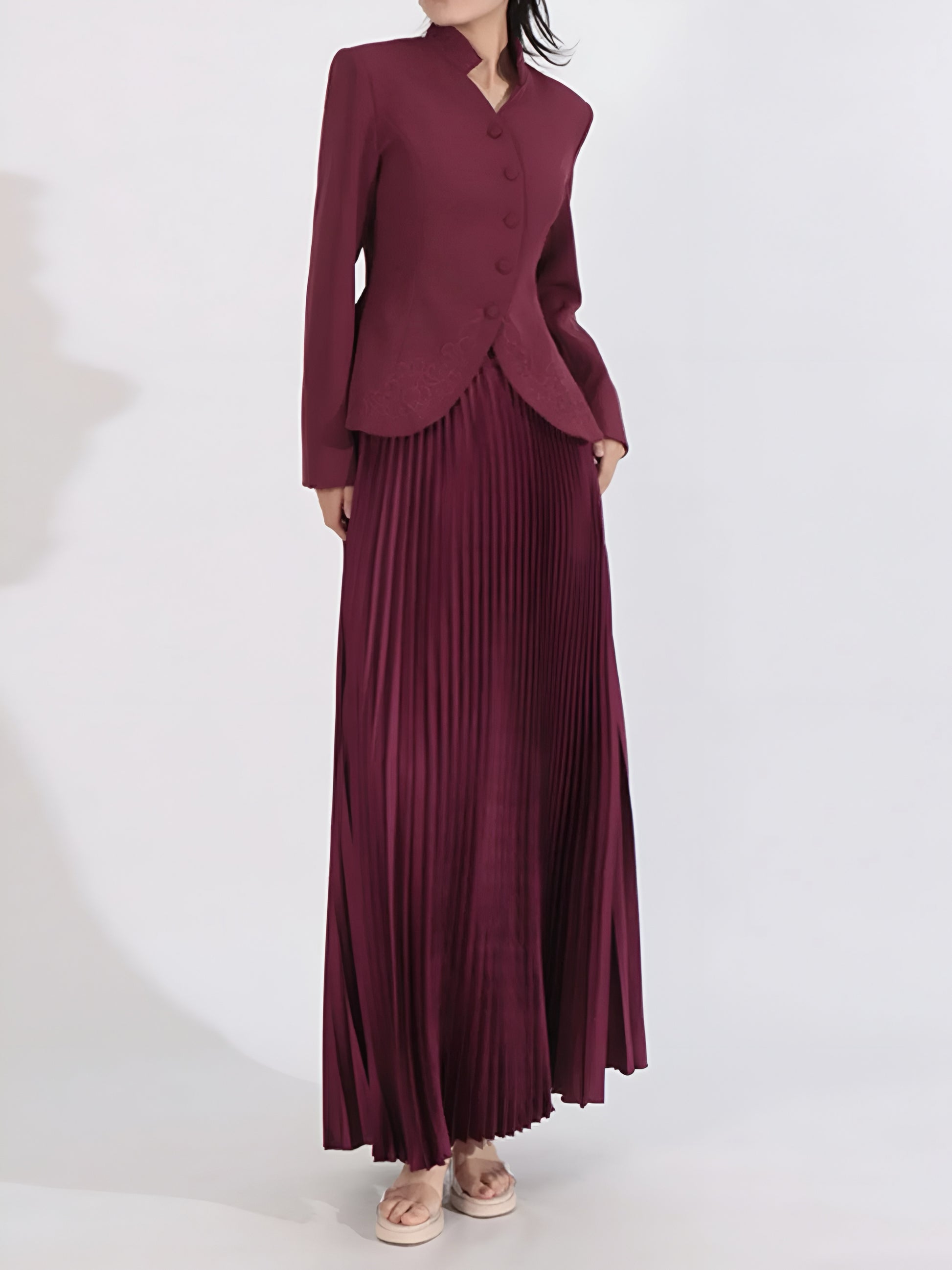 Woman posing in a structured embroidered jacket with pleated maxi skirt on a white background