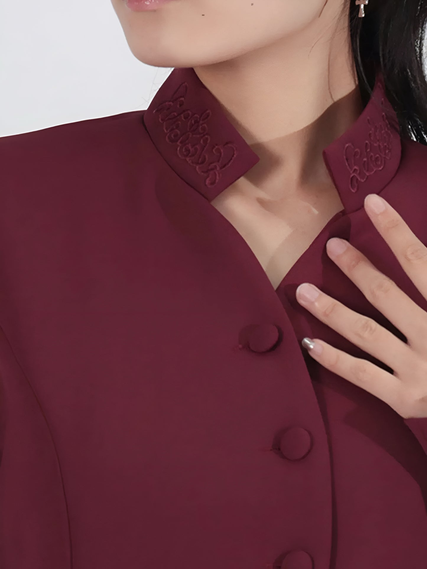 Close-up of neckline of buttoned long sleeve suit jacket in burgundy coat intricate detailing on the collar.