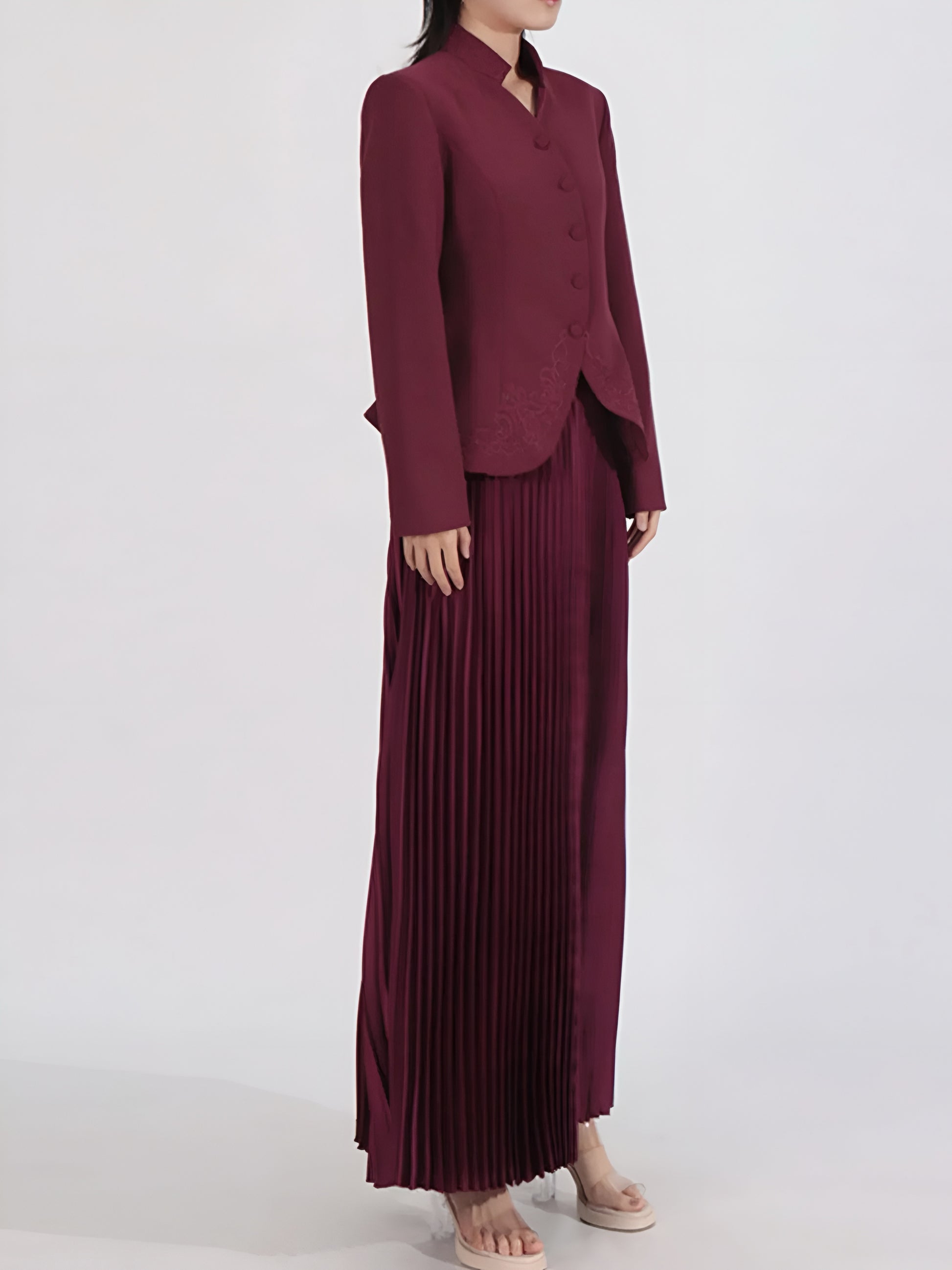 Side view of woman wearing  two piece suit set with a jacket and pleated skirt on a white background