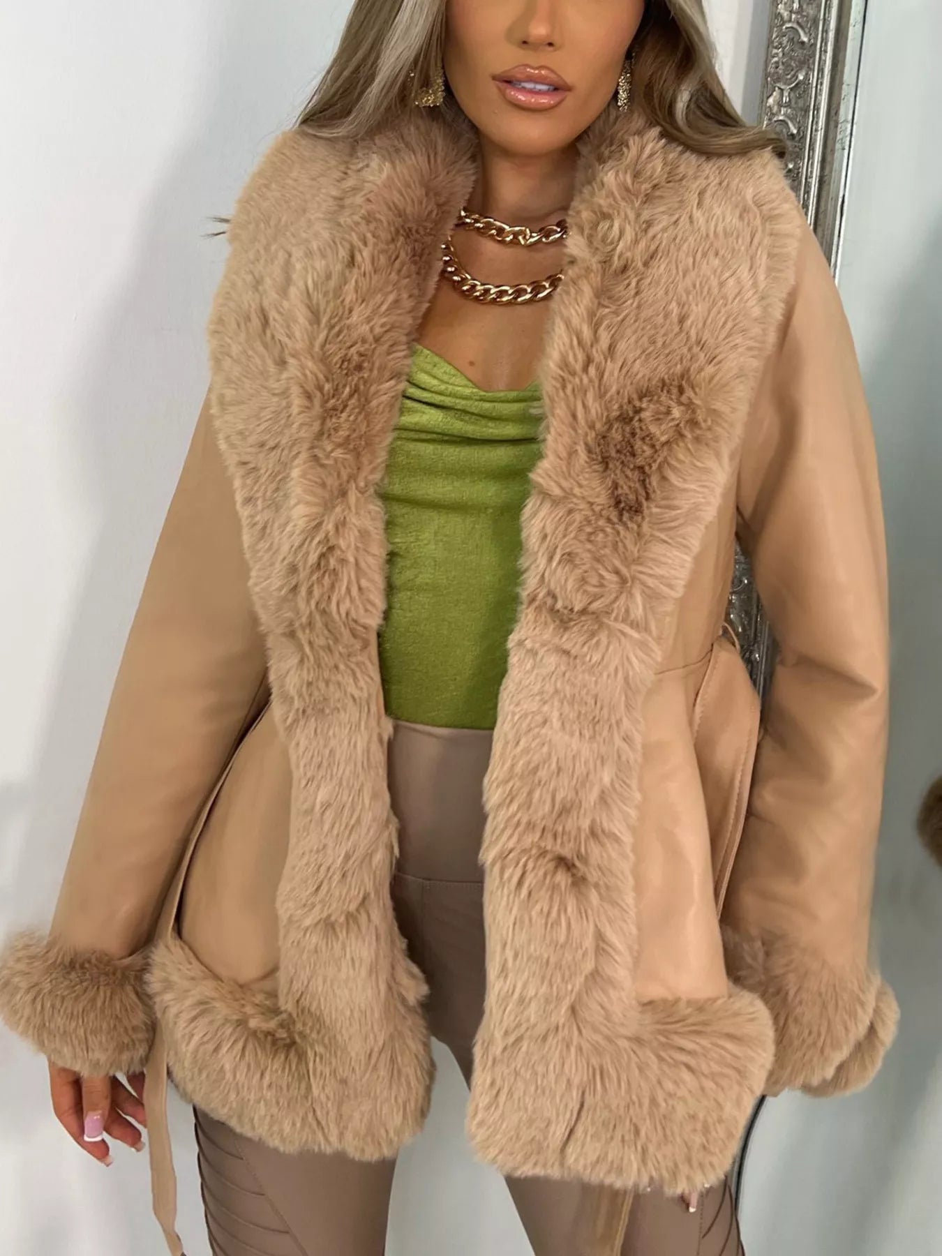 Woman wearing a beige coat with faux fur trim, standing against a white background