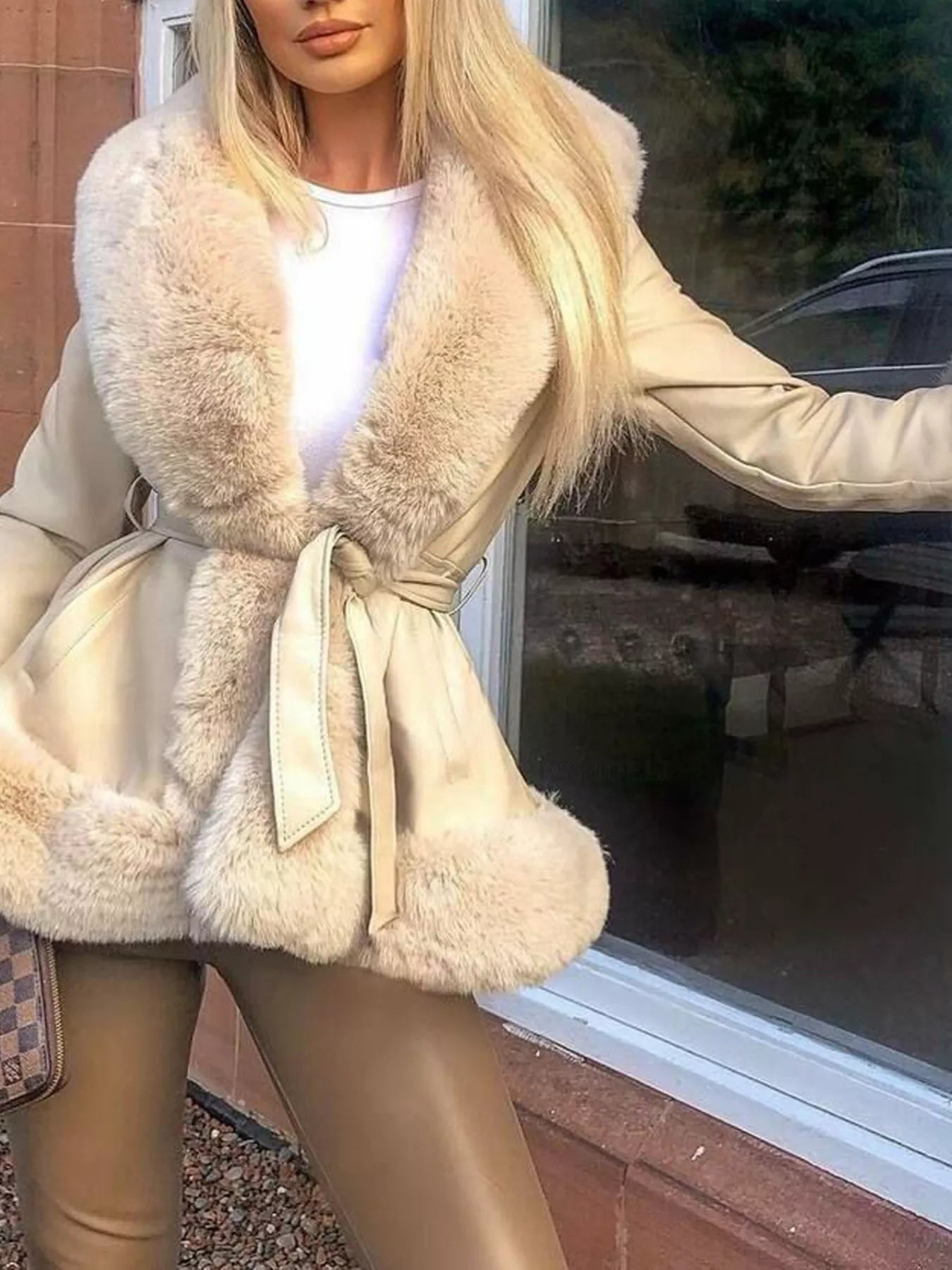 woman wearing a beige coat with fur trim in front of a window.