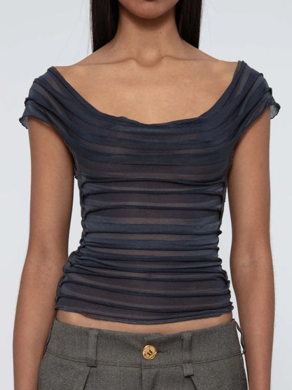 Woman wearing a dark gray ruched top and gray pants on a white background