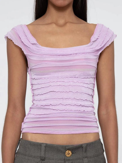 Woman wearing a light pink ruched sleeveless top with a plain background