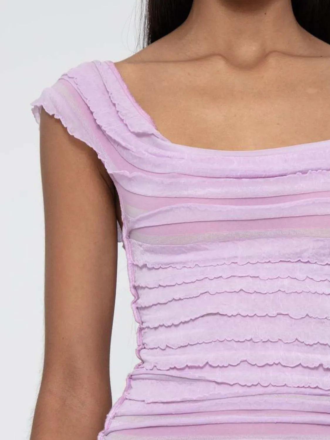 Close-up of a woman wearing a light pink ruched sleeveless top with ruffled details.