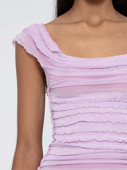 Close-up of a woman wearing a light pink ruched sleeveless top with ruffled details.