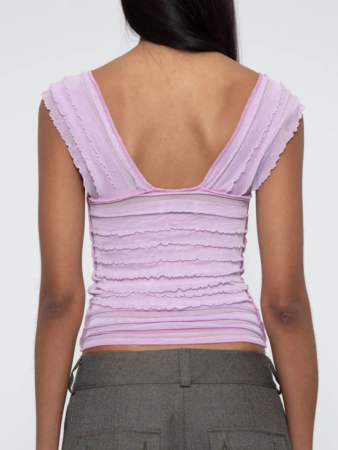 woman wearing a light pink ruffled ruched sleeveless top back view with a plain background