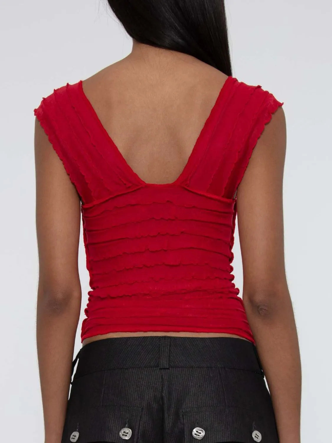 woman wearing a red  ruched sleeveless top with a V-back and ruched details on a plain background