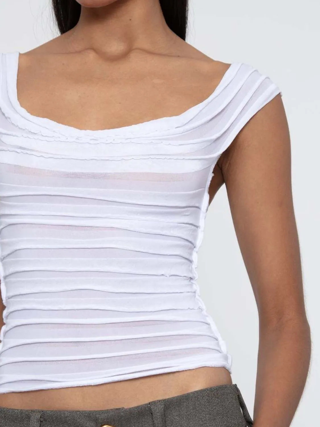 White off-shoulder ruched sleeveless top worn by a woman on a plain background