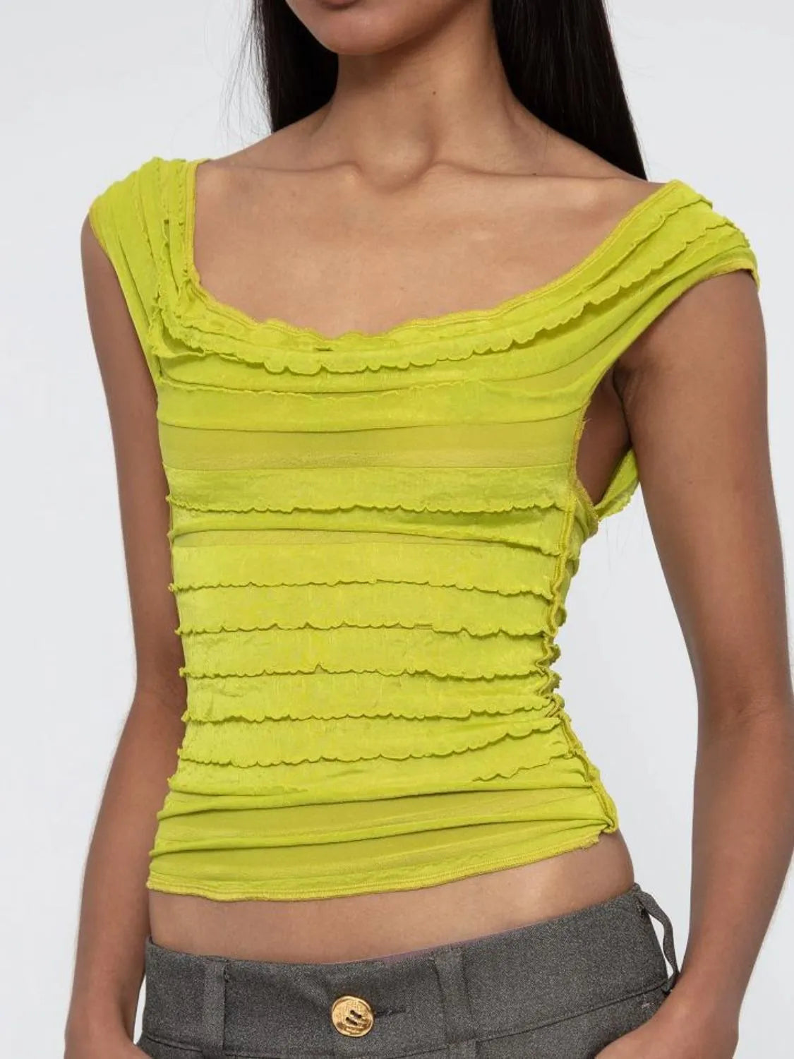 Woman wearing a yellow green ruched sleeveless top with a plain background
