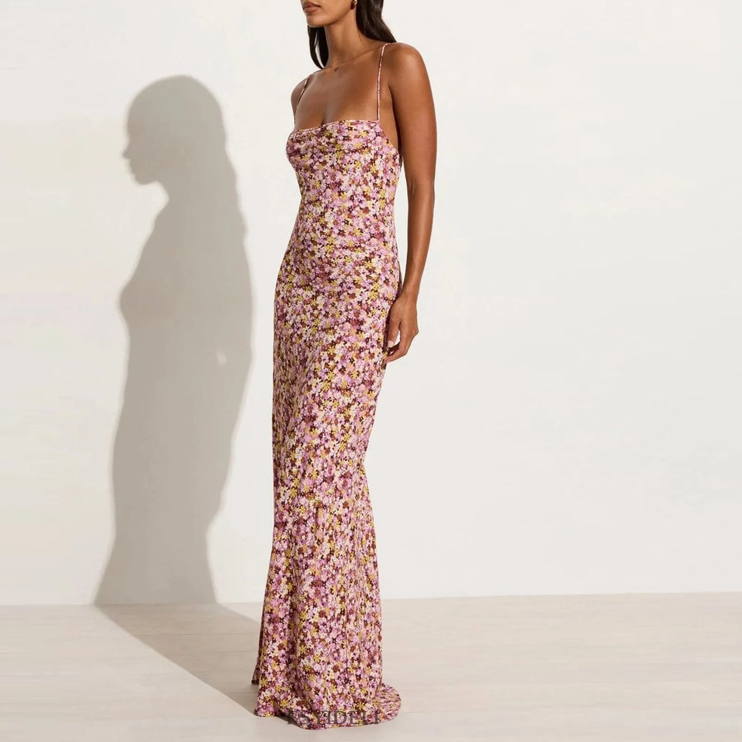 Side view of woman wearing a purple floral cami backless maxi  dress against a plain background