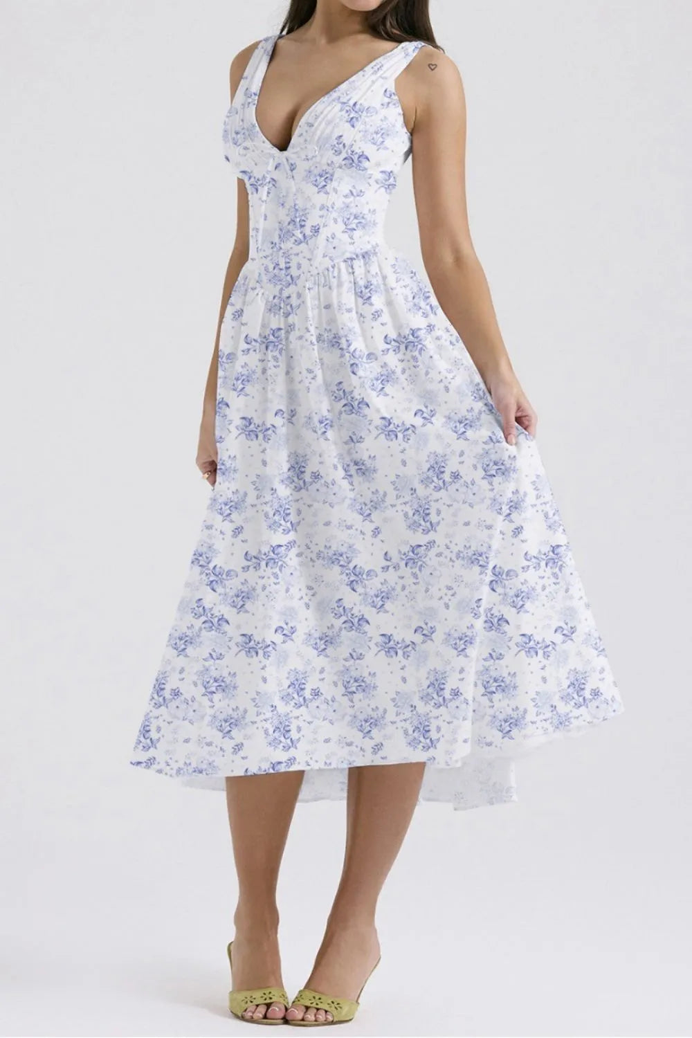Woman wearing a flowy white and blue floral sleeveless midi dress with pockets on a white background