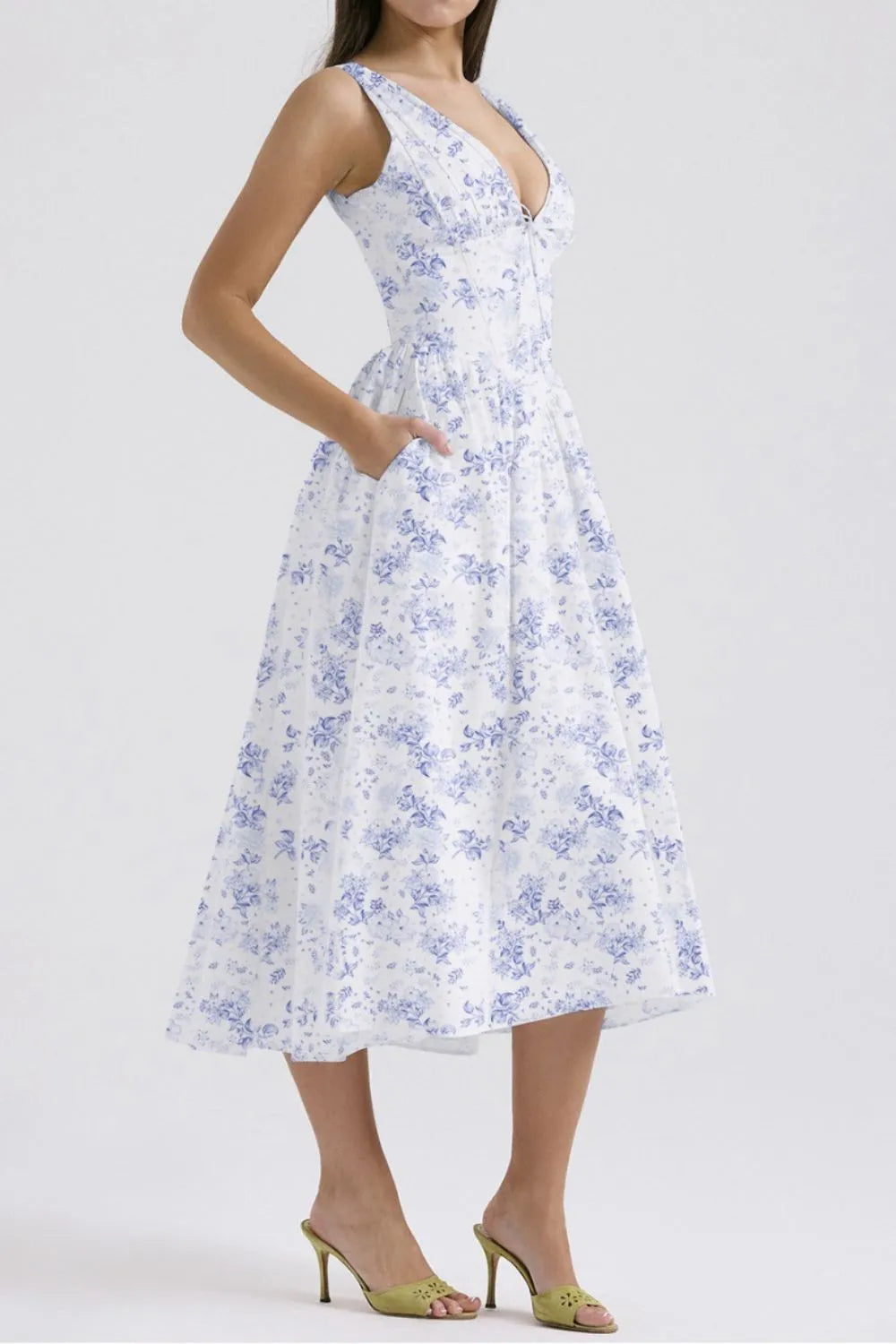 Side view of woman wearing a white with blue floral pattern v-neck sleeveless midi dress with pockets on a white background