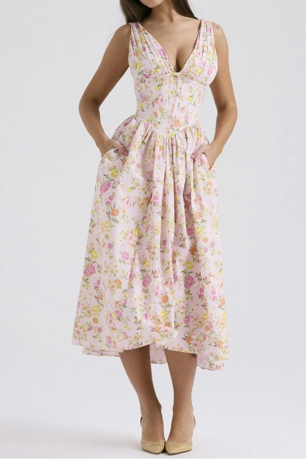 Woman wearing a pink floral v-neck midi dress with pockets on a white background