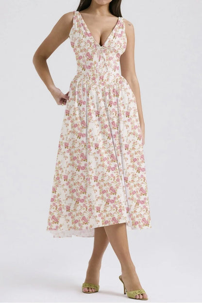 Woman wearing a white and pink floral flowy sleeveless v-neck midi dress with pockets on a white background