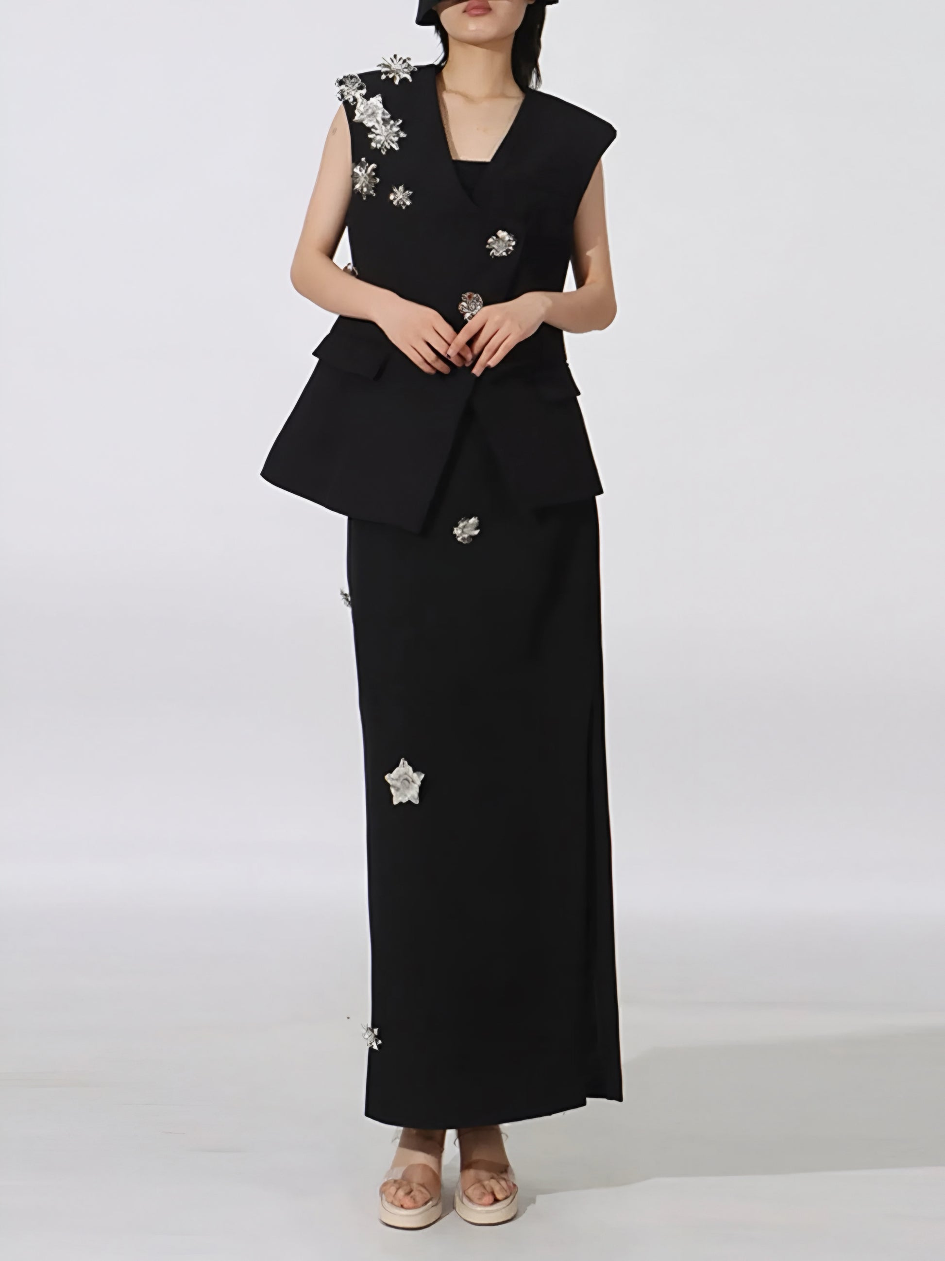 Woman wearing a black Designer-inspired two-piece co-ord with tailored vest and maxi skirt with floral embellishments on a white background
