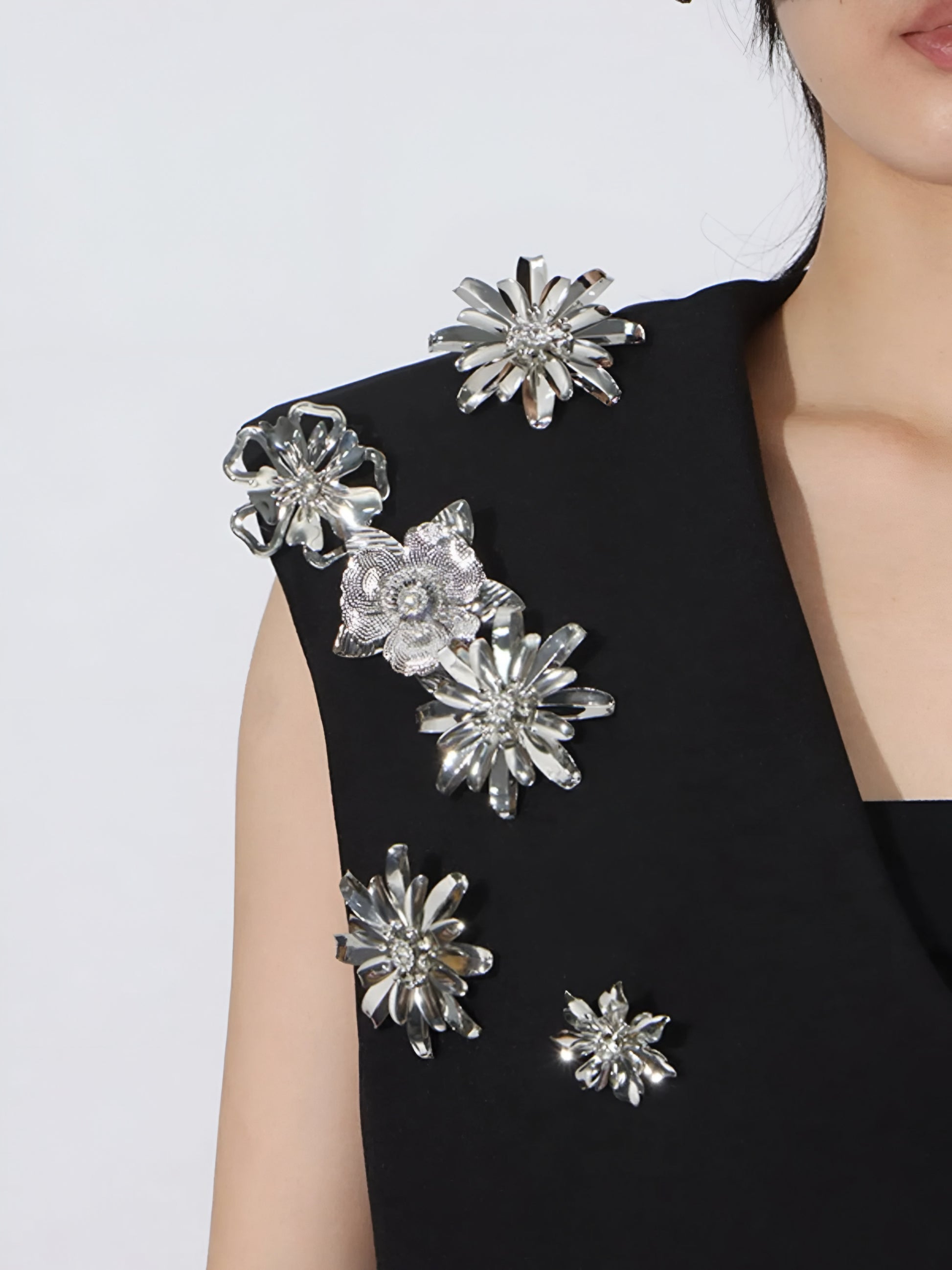 close up of sleeveless luxury black vest with silver floral embellishments on a white background