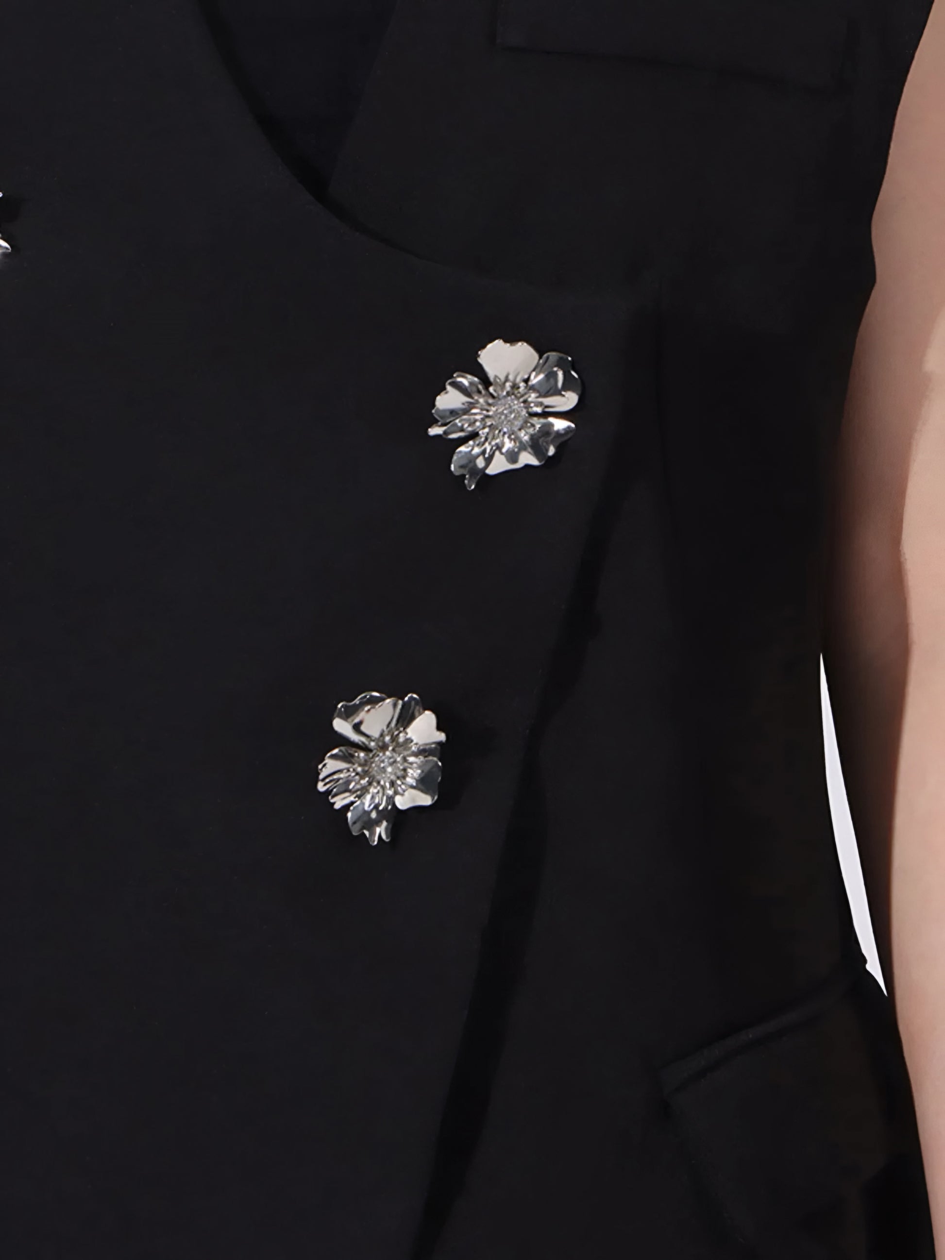 Close-up of a black sleeveless blazer with silver rhinestone floral embellishment.