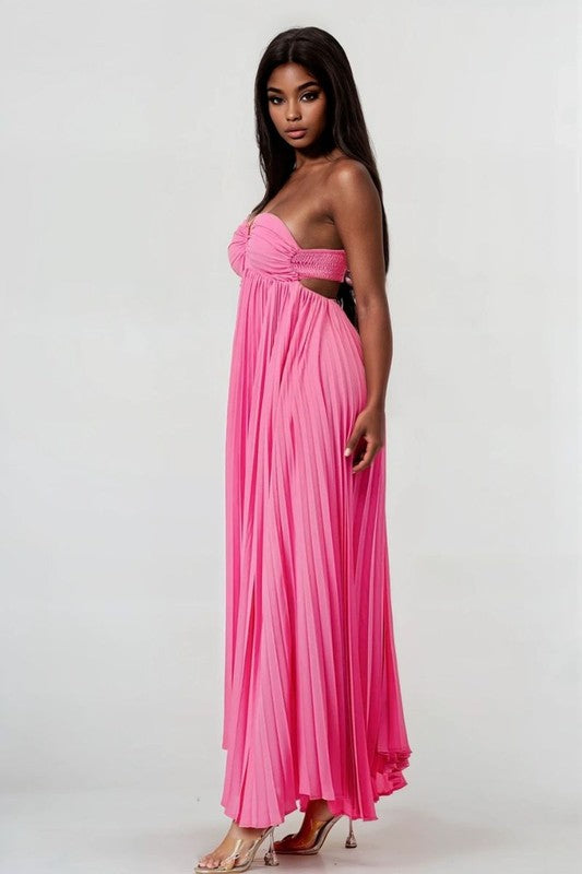 side view of woman wearing a flowy pink pleated maxi dress with halter neckline and open back