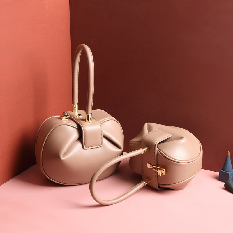 two beige / apricot  leather dumpling handbag with a buckle closure and a single handle, displayed against a two-tone background 