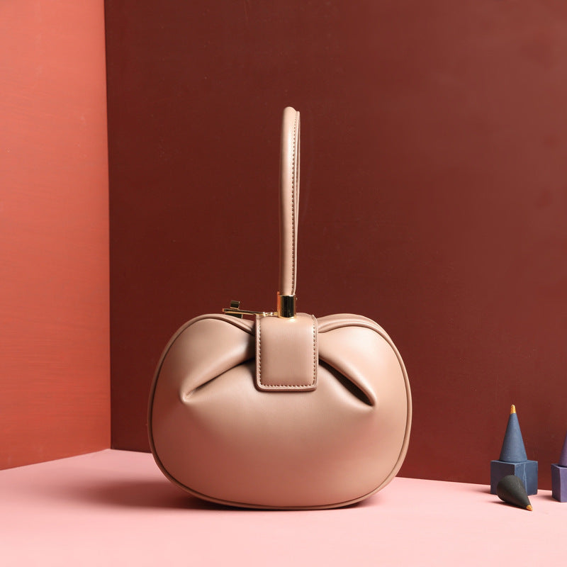A beige / apricot  leather dumpling handbag with a buckle closure and a single handle, displayed against a two-tone background 