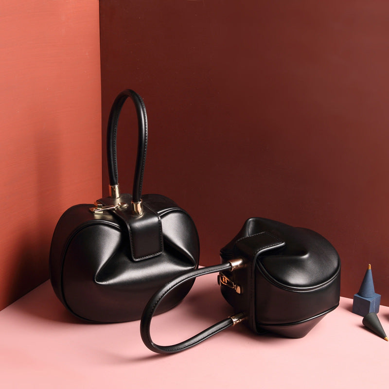 two black leather dumpling handbag with a buckle closure and a single handle, displayed against a two-tone background 