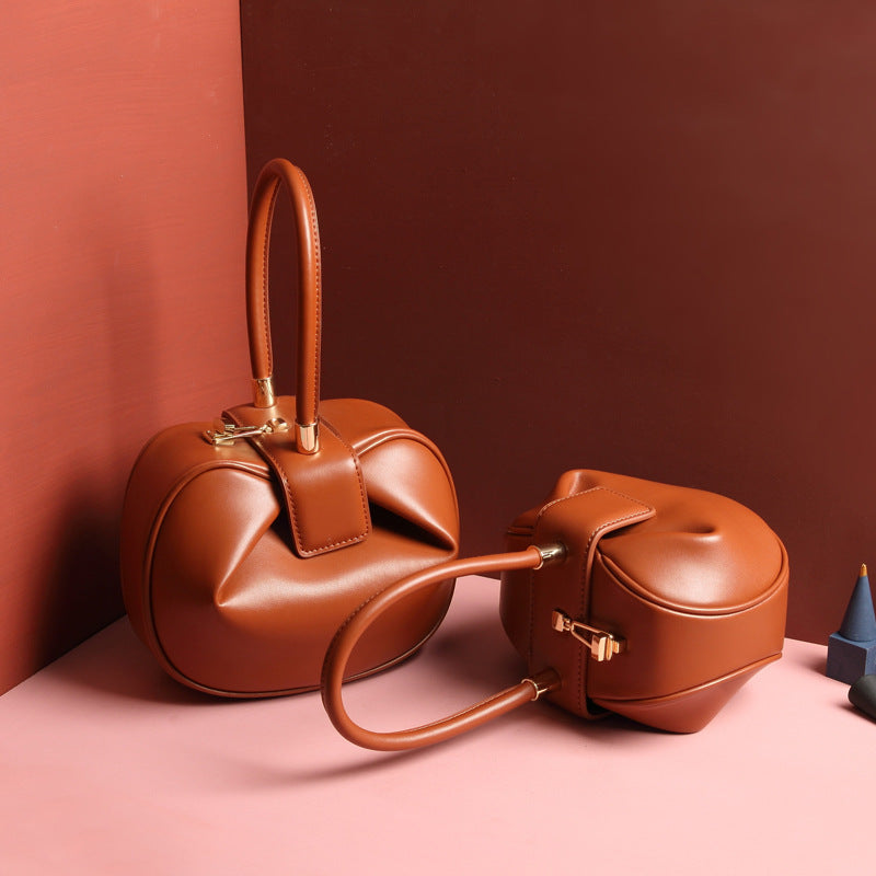 two brown leather dumpling handbag with a buckle closure and a single handle, displayed against a two-tone background 