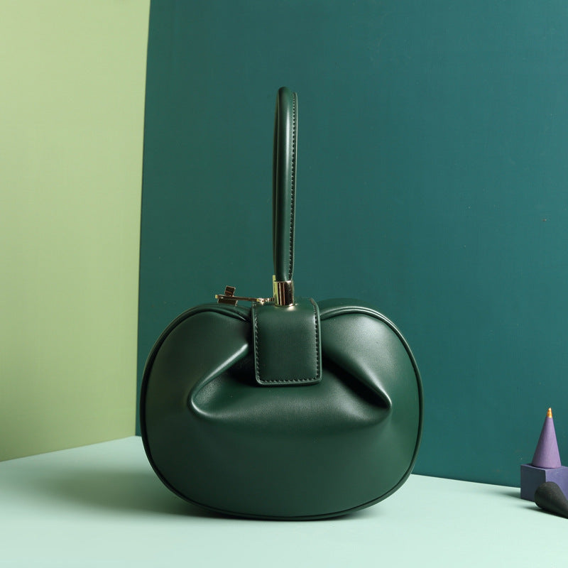 A green leather dumpling handbag with a buckle closure and a single handle, displayed against a two-tone background 