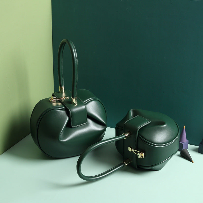 two green leather dumpling handbag with a buckle closure and a single handle, displayed against a two-tone background 