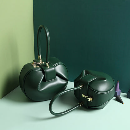 two green leather dumpling handbag with a buckle closure and a single handle, displayed against a two-tone background 