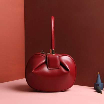 A red leather dumpling handbag with a buckle closure and a single handle, displayed against a two-tone background 